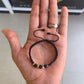 Pulsera unisex de hilo negro con cuentas negras y balines de oro 18K, sostenida frente al logo de Brillo Encanto.