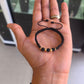 sobre la palma de la mano: Pulsera de balines de oro 18K y cuentas negras sobre la palma de una mano, con tejido negro y cordones ajustables.