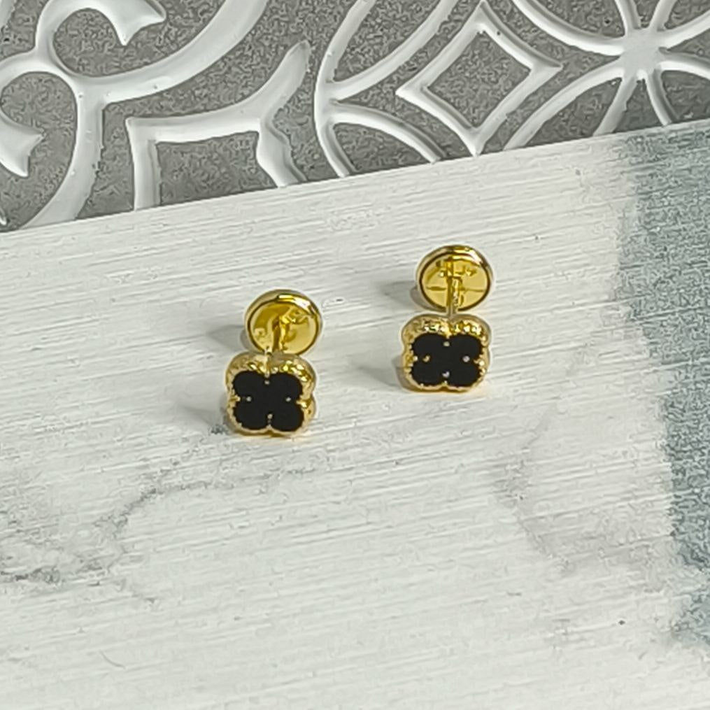 Aretes trébol negro en oro laminado 18K para mujer sobre fondo elegante. Diseño delicado y moderno, ideales para regalo o uso diario. Antialérgicos y con rosca de seguridad.