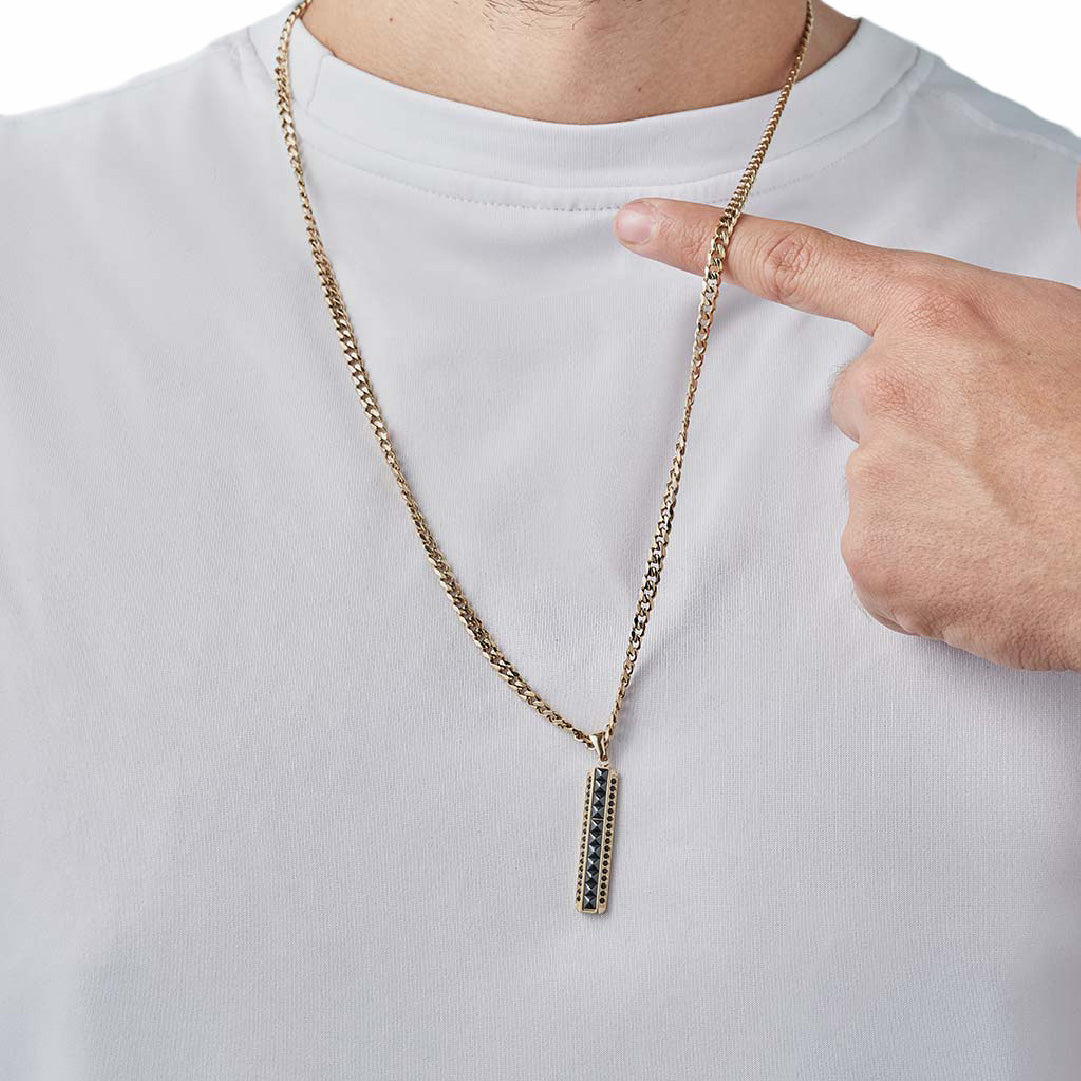 Hombre señalando dije barra oro laminado 18k con piedras negras sobre camiseta blanca