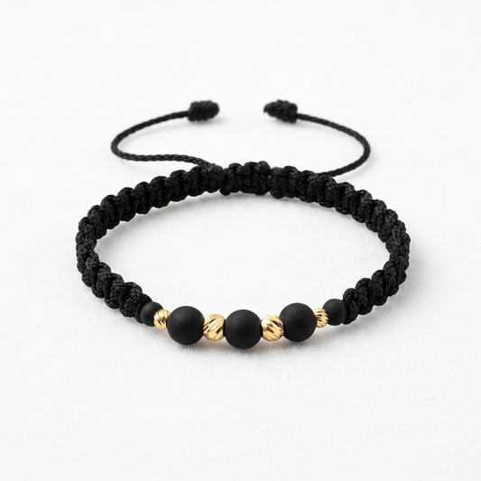 Pulsera unisex de hilo negro tejido con cuentas negras y balines de oro 18K, con cierre ajustable.